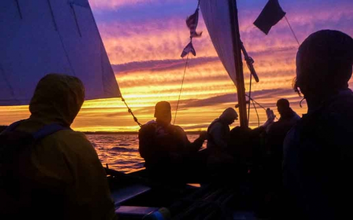 the silhouette of a group of people on a sailboat at sunset